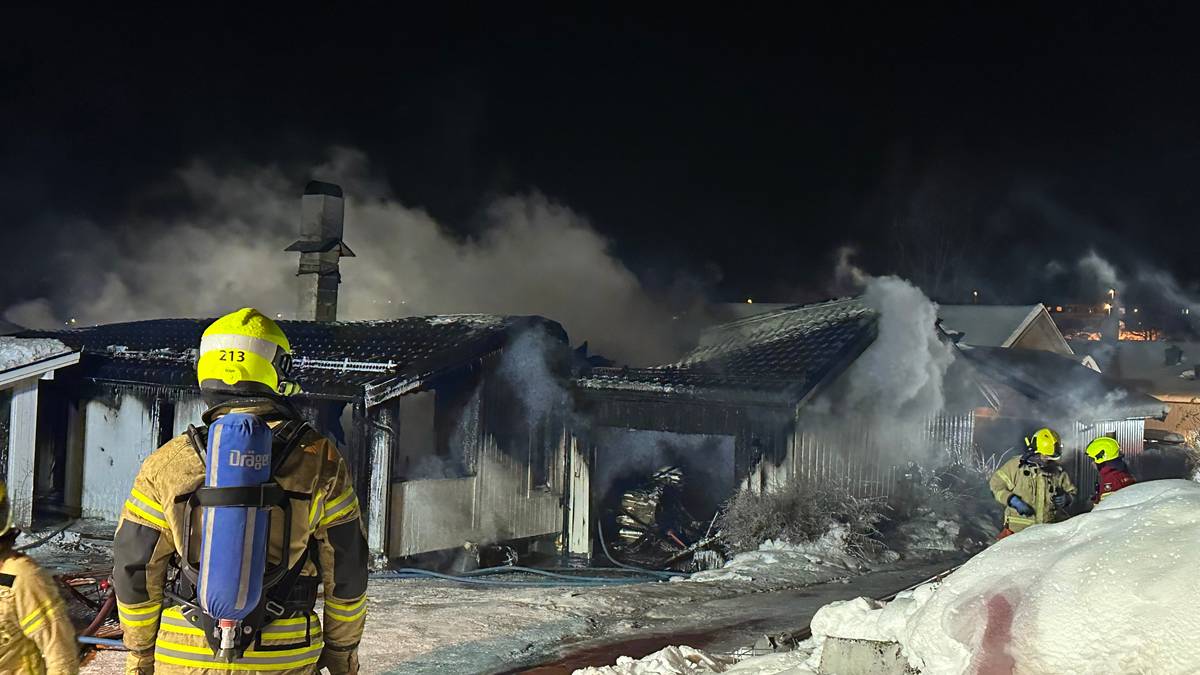Brannmenn arbeider for å slukke en brann i en enebolig om natten. Røyk stiger fra de brente områdene av bygningen. Snø dekkes bakken rundt, og det er svake lys fra nabohusene i bakgrunnen. Brannmenn med hjelmer og brannvernutstyr er synlige i bildet. (Bildebeskrivelsen er laget av en KI-tjeneste)