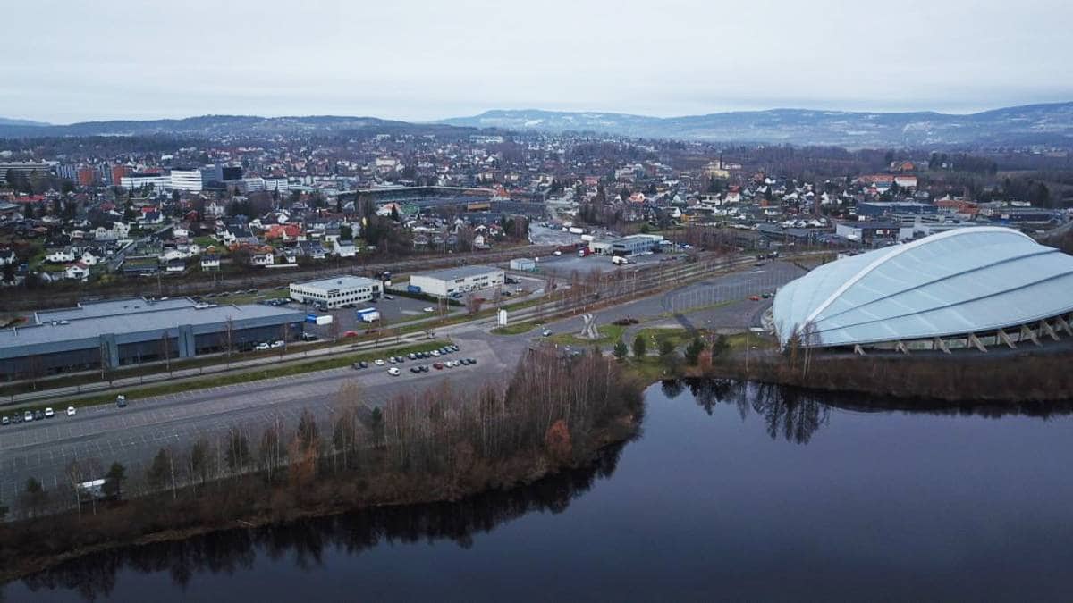 Bildet viser en oversiktsvisning av et urbant område med bygninger og veier i et grått vær. Til høyre synes en stor kuppelstruktur, sannsynligvis en idrettshall, som ligger nær en innsjø. Bakgrunnen viser et variert boligområde med hus i forskjellige stilarter og høyder. Området er preget av bilvei og parkeringsplasser, men det er få synlige mennesker.