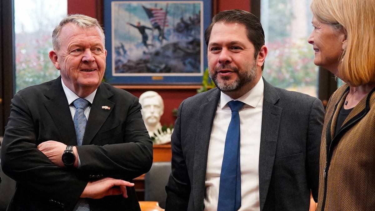 Tre personer står tett sammen i et rom. Den ene mannen har på seg en sort jakke med en skjorte og slips, mens den andre mannen er iført en mørk blazer og hvit skjorte med slips.