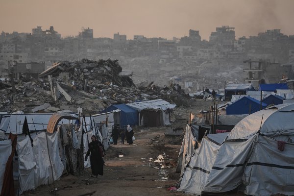 Palestinians walk past a tent camp amid buildings destroyed by Israeli air and ground operations in Gaza City Tuesday, Jan. 6, 2026. (AP Photo/Jehad Alshrafi)
