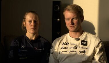 To personer sitter på en sofa i et rom med varmt, naturlig lys. De er kledd i sportsklær, og det er synlig elektronisk utstyr i bakgrunnen. Den ene personen har langt hår, mens den andre har kort hår. Begge ser direkte mot kameraet. (Bildebeskrivelsen er laget av en KI-tjeneste)