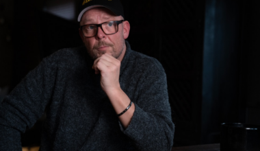 Mann med skyggelue støtter haka mot venstre neve og ser ettertenksom ut