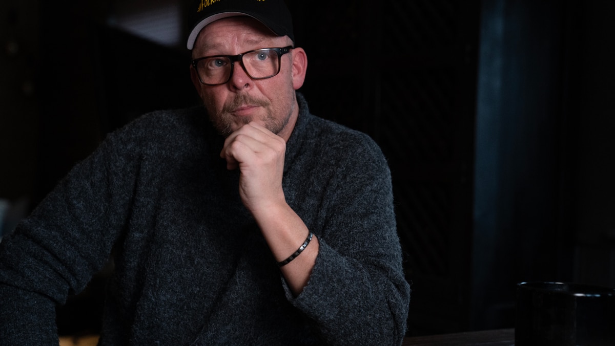 Mann med skyggelue støtter haka mot venstre neve og ser ettertenksom ut