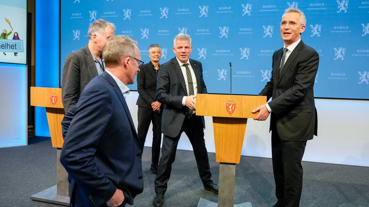 Fem personer står foran podiumer i en offisiell setting. Noen av dem er i samtale, mens en annen ser på. Det er skilting med offentlige symboler i bakgrunnen, og blå vegger danner en nøytral kontekst. Rommet har belysning som fremhever scenen, som virker tilrettelagt for en pressemelding. (Bildebeskrivelsen er laget av en KI-tjeneste)