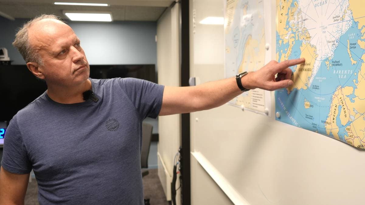 En mann i t-skjorte peker på Grønland på et kart over Arktis.
