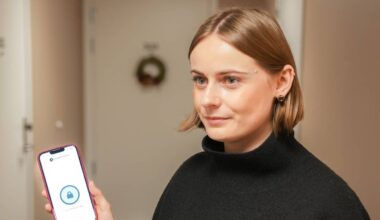 en ung kvinne står i en gang i et bygg og holder en telefon opp med den ene hånda