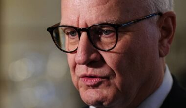 Kristian Harpviken kledd i mørk dress og slips. I bakgrunnen er det uskarpe lys og elementer som gir en formell atmosfære. Bildet fokuserer på mannen og hans kroppsspråk. (Bildebeskrivelsen er laget av en KI-tjeneste)