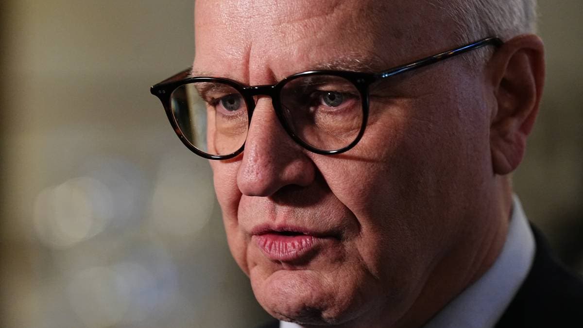 Kristian Harpviken kledd i mørk dress og slips. I bakgrunnen er det uskarpe lys og elementer som gir en formell atmosfære. Bildet fokuserer på mannen og hans kroppsspråk. (Bildebeskrivelsen er laget av en KI-tjeneste)