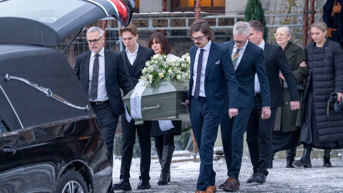 En gruppe personer bærer en kiste, dekorert med blomster, ut fra en kirke. De fleste av dem er ikledd formelle klær, og handlingen skjer på en vinterdag med snø på bakken. I bakgrunnen kan man se en svart bil, antagelig en begravelsesbil, parkert ved inngangen. En del tilskuere står på siden av veien og observerer bevegelsene. (Bildebeskrivelsen er laget av en KI-tjeneste)