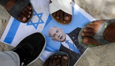 Flere mennesker står med føttene på en utskrevet plakat med det israelske flagget. Plakaten er delvis dekket til.