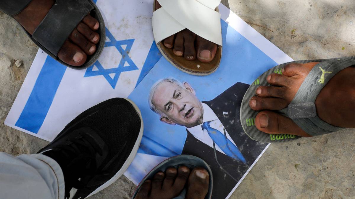 Flere mennesker står med føttene på en utskrevet plakat med det israelske flagget. Plakaten er delvis dekket til.