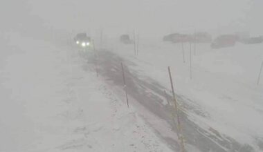 Snøfokk og dårlig sikt på en fjellvei med biler i bakgrunnen