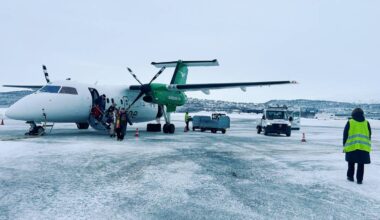 Widerøe fly står på bakken og passasjerer kommer ut på flyplassen i Bodø. En bakkeansatt med gul vest går i forgrunn.