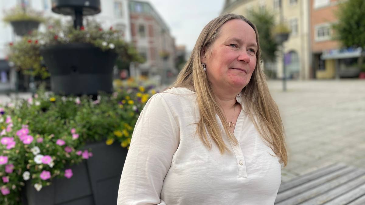 En kvinne sitter på en benk ute. Hun har langt blondt hår, og har på seg en hvit bluse. Hun ser ut mot landskapet.