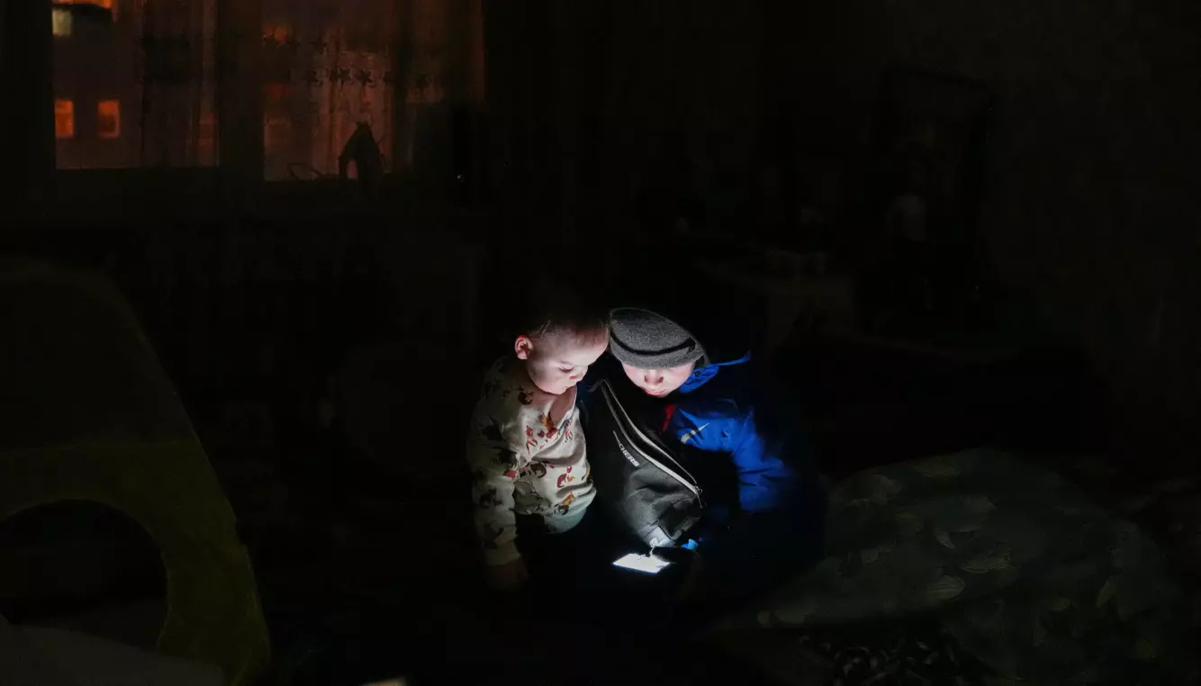 Daniil Dolotov (11) og broren Bohdantsjyk (18 måneder) leker med mobilen i familiens leilighet i Kyiv etter at strømmen gikk som følge av et russisk angrep 2. februar. Foto: Sergej Grits / AP / NTB