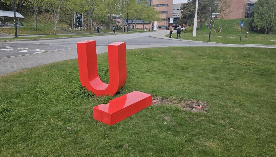Rød skulptur formet som en U står på et grønt gressområde ved en vei.