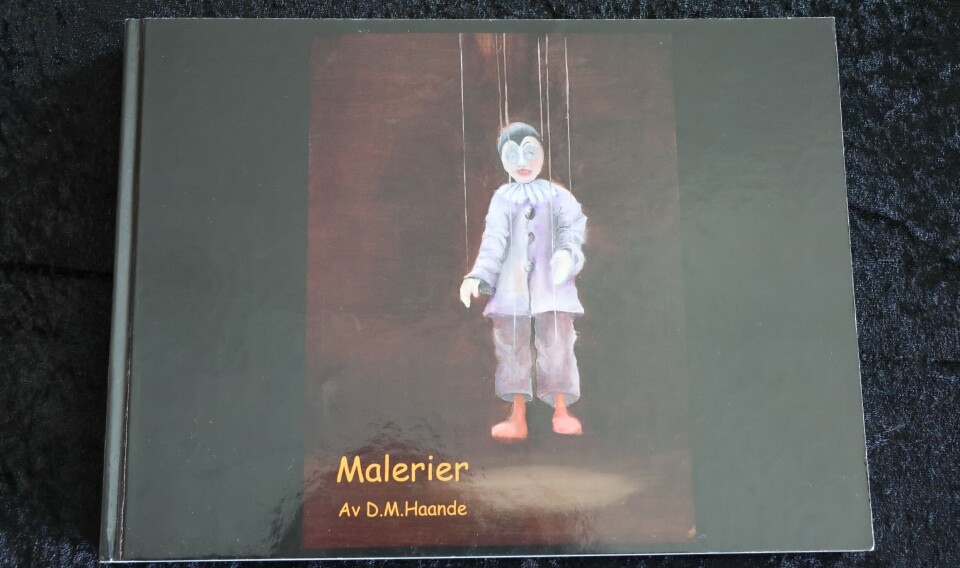 En bok med mørkt omslag og et bilde av en stående figur ligger på et teppe.