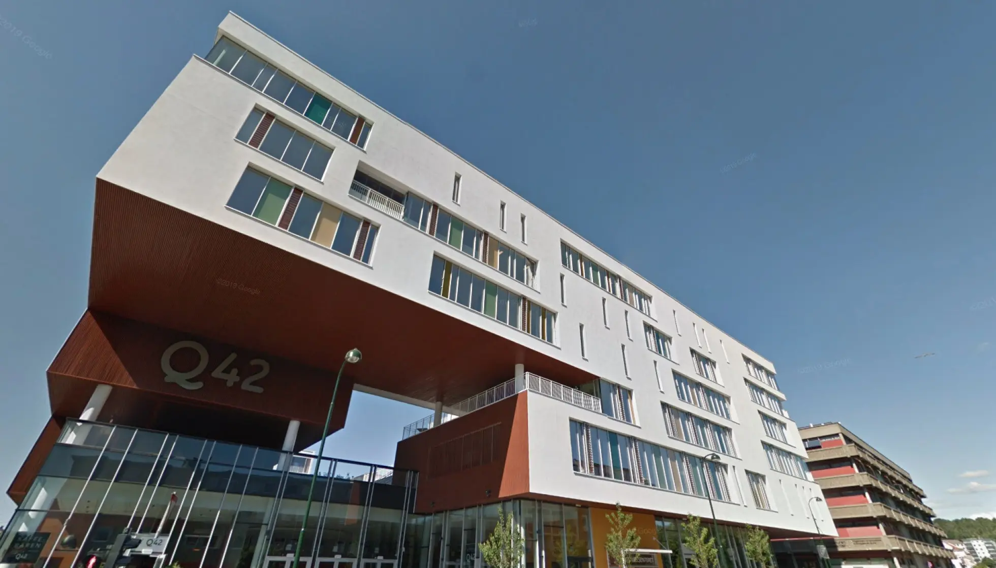Moderne bygg med Q42-logoen på fasaden sett fra gateplan på en klar dag.