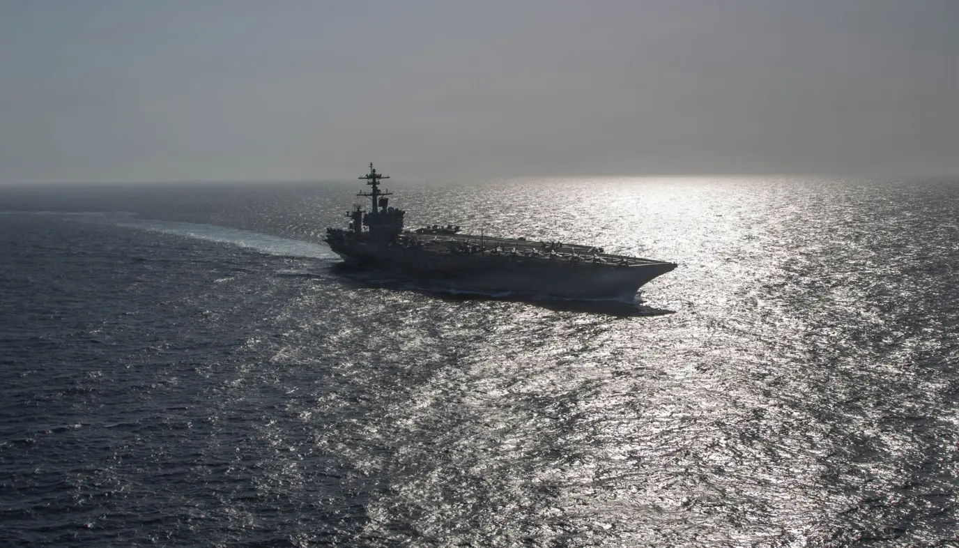 Amerikansk hangarskip seiler på åpent hav med solglitter på vannflaten.