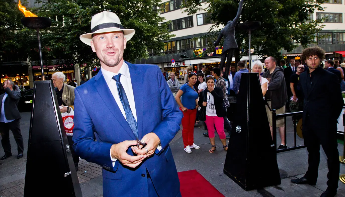 Dagfinn Lyngbø i blå dress og hatt står på rød løper foran Chat Noir i Oslo.