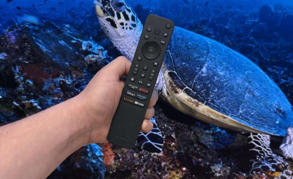 Pilot Sony BRAVIA 8 II trzymany w dłoni przed ekranem OLED z materiałem 4K HDR