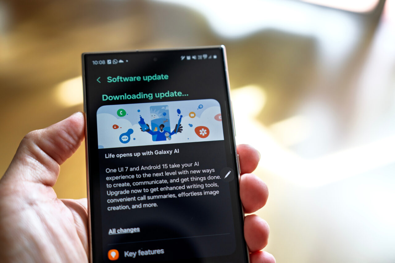 Smartfon Samsung trzymany w dłoni z wyświetlaczem pokazującym ekran pobierania aktualizacji oprogramowania z informacją o funkcjach Galaxy AI w One UI 8 i Android 15.