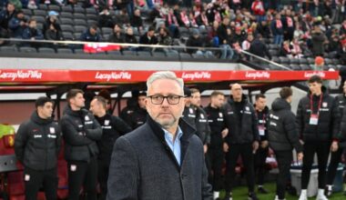 Mężczyzna w okularach i koszuli z krótkim rękawem na trybunach stadionu, w tle rozmyci kibice i elementy stadionu sportowego.