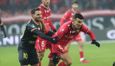 Bramkarz ubrany w niebieski strój łapie piłkę podczas meczu piłki nożnej, na trybunach widać rozmytą publiczność.