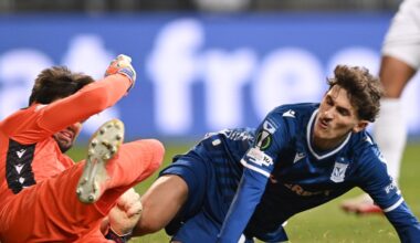 W akcji sportowej kilku piłkarzy na murawie stadionu, zawodnik w niebieskim stroju prowadzi piłkę, ścigany przez zawodników w białych strojach z logo INEOS, w tle rozmazana sylwetka bramkarza.