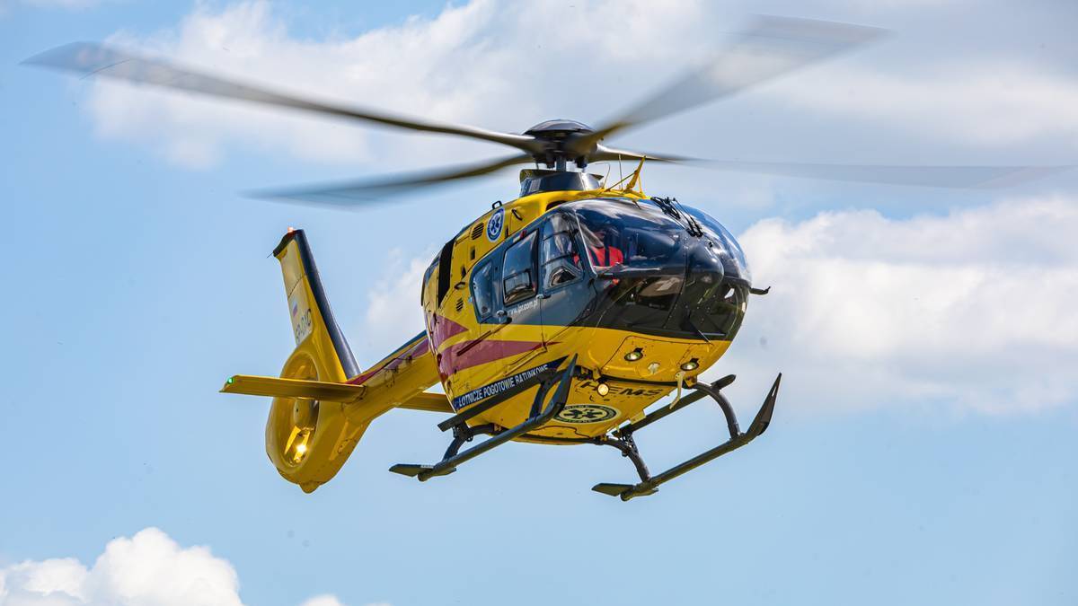 Żółty helikopter medyczny w locie na tle błękitnego nieba z chmurami.