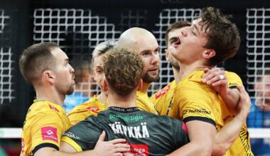 Siatkarze w żółtych strojach zespołowo świętują zwycięstwo, przytulając się do siebie na boisku.