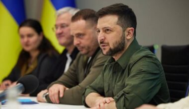 Prezydent Ukrainy Wołodymyr Zełenski siedzi przy stole podczas spotkania, przemawia, obok niego siedzą inni mężczyźni i kobieta.