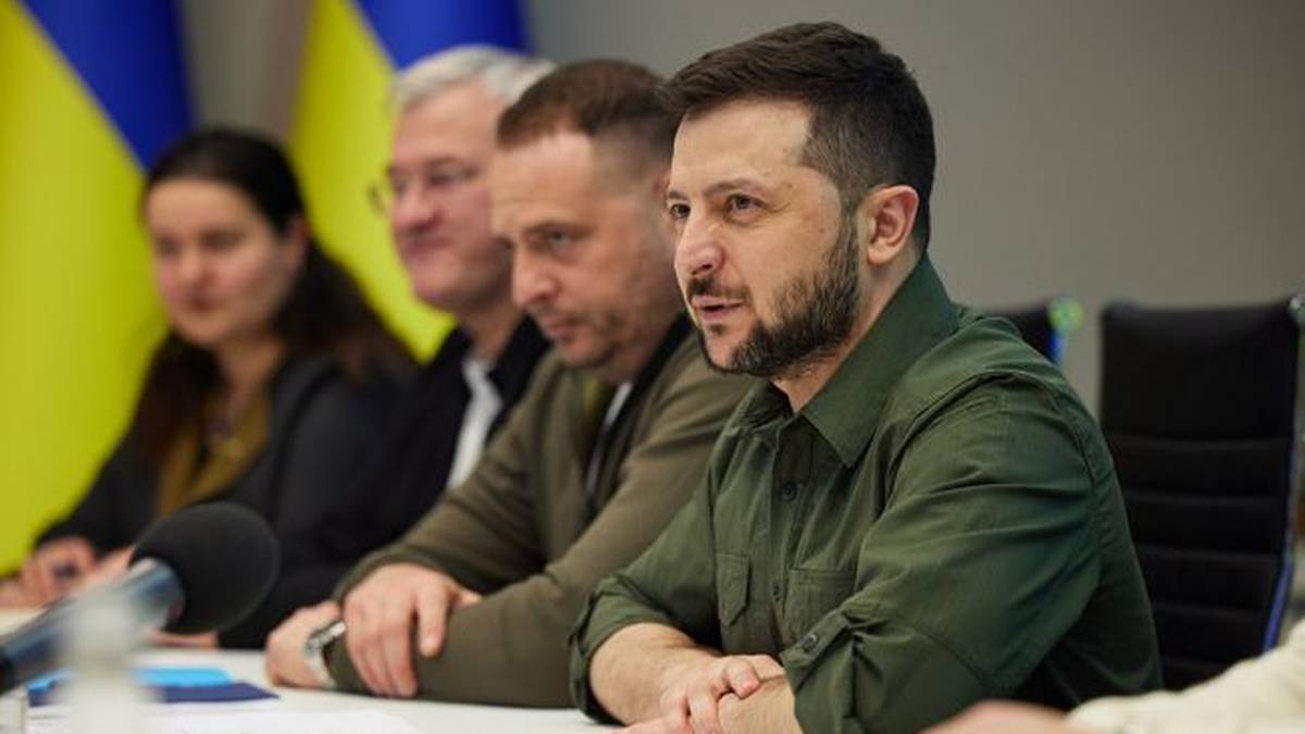 Prezydent Ukrainy Wołodymyr Zełenski siedzi przy stole podczas spotkania, przemawia, obok niego siedzą inni mężczyźni i kobieta.