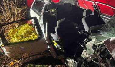 Uszkodzony biały samochód osobowy po wypadku drogowym, widoczne otwarte drzwi i wnętrze pojazdu.