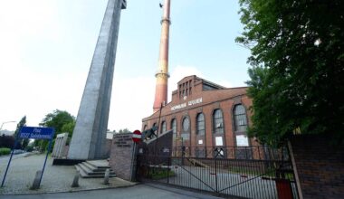Monumentalny monument krzyża obok ceglanego budynku przemysłowego z kominem w Katowicach.
