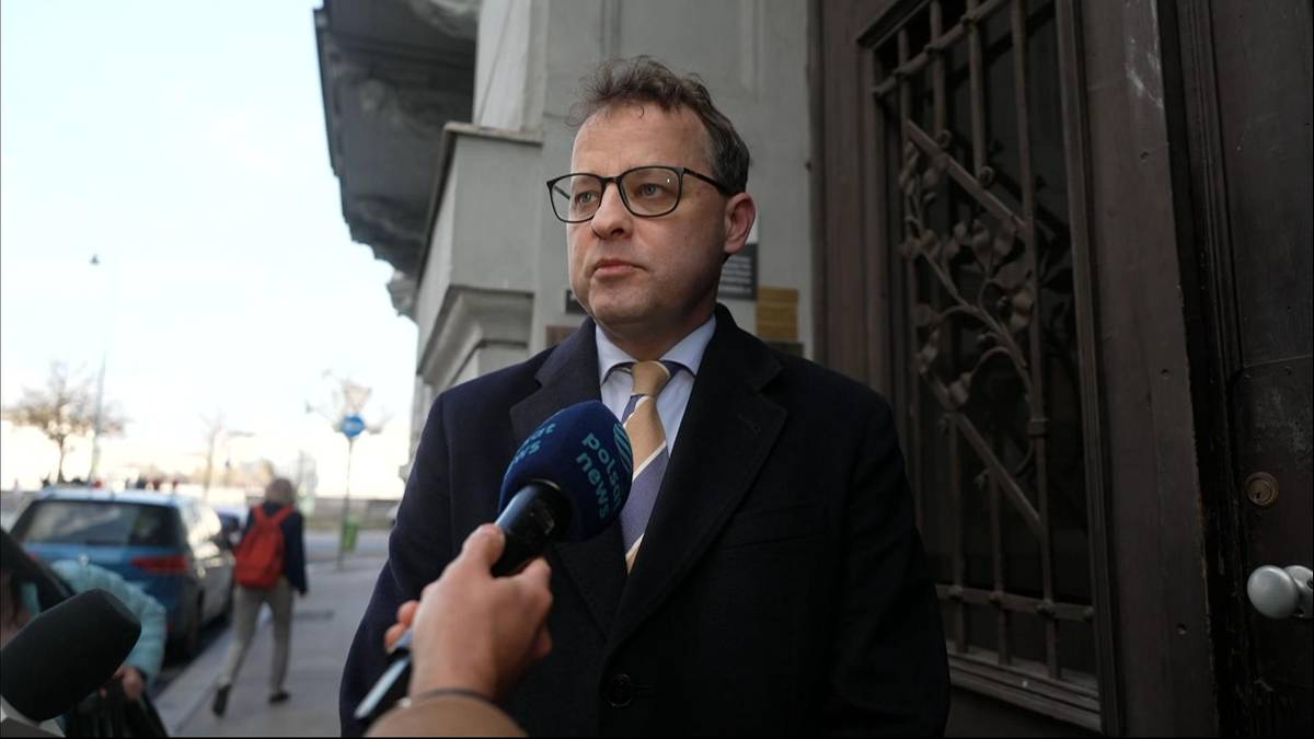 Marcin Romanowski w okularach i ciemnym płaszczu udziela wywiadu dziennikarzowi Polsat News.