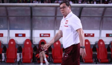 Trener reprezentacji Polski w piłce nożnej, Michał Probierz, ubrany w białą koszulkę polo i bordowe spodenki, idzie wzdłuż ławki rezerwowych.