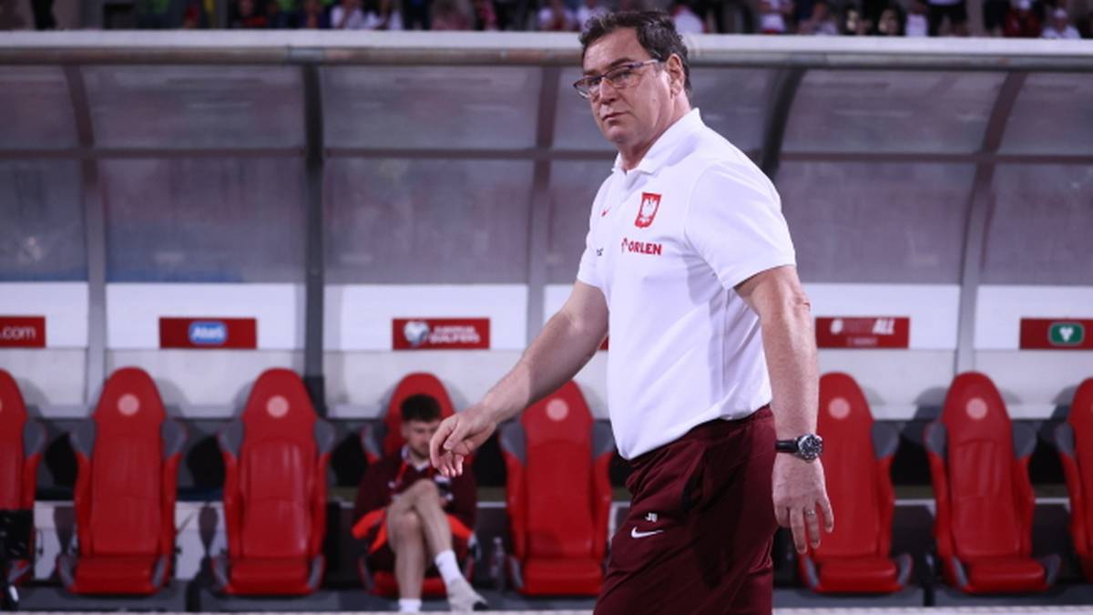 Trener reprezentacji Polski w piłce nożnej, Michał Probierz, ubrany w białą koszulkę polo i bordowe spodenki, idzie wzdłuż ławki rezerwowych.