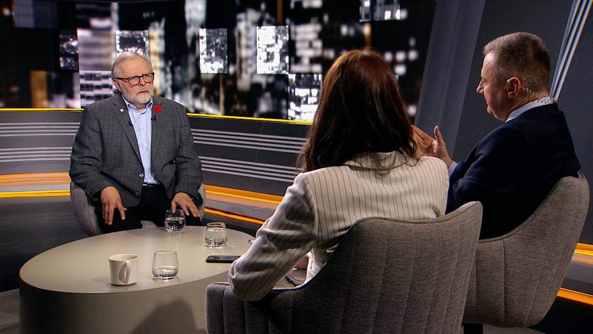 Profesor Szymon Malinowski siedzi przy stole w studiu telewizyjnym, rozmawiając z kobietą i mężczyzną. Na stole stoją szklanki i filiżanki.