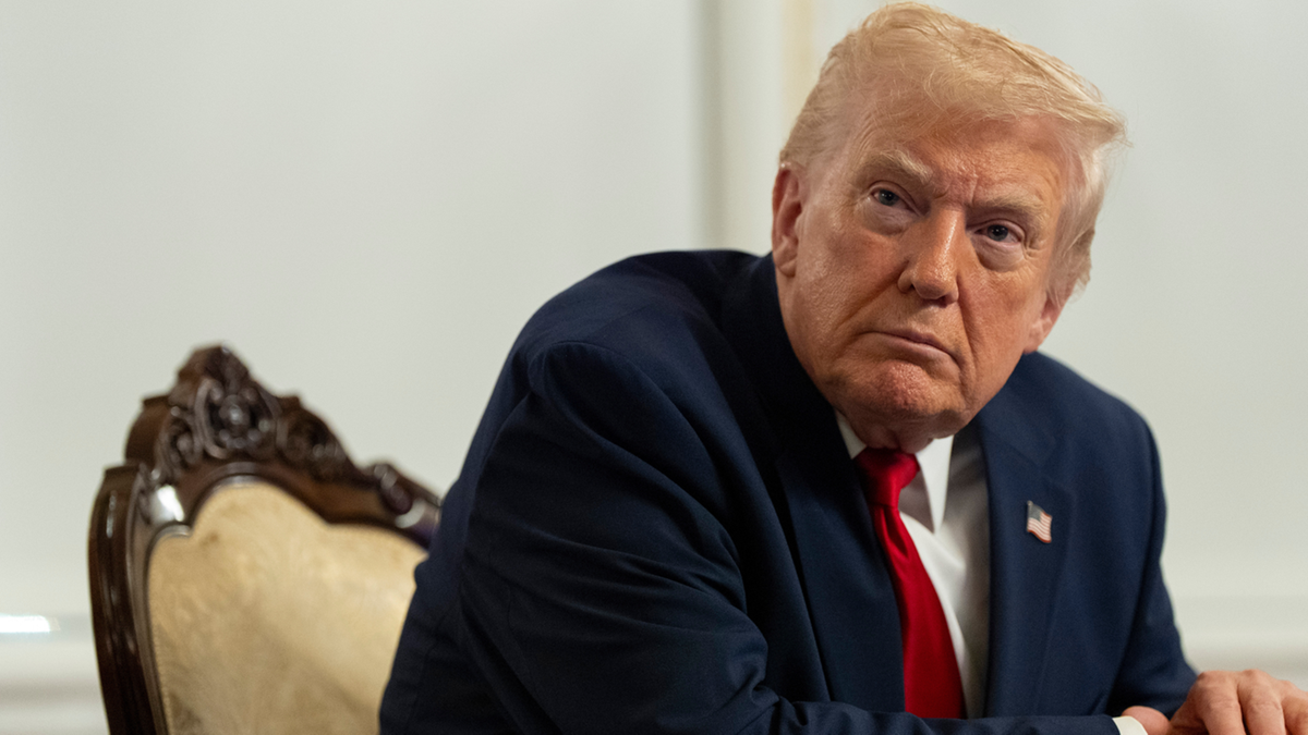 Donald Trump siedzi na krześle, patrząc w bok z poważnym wyrazem twarzy.