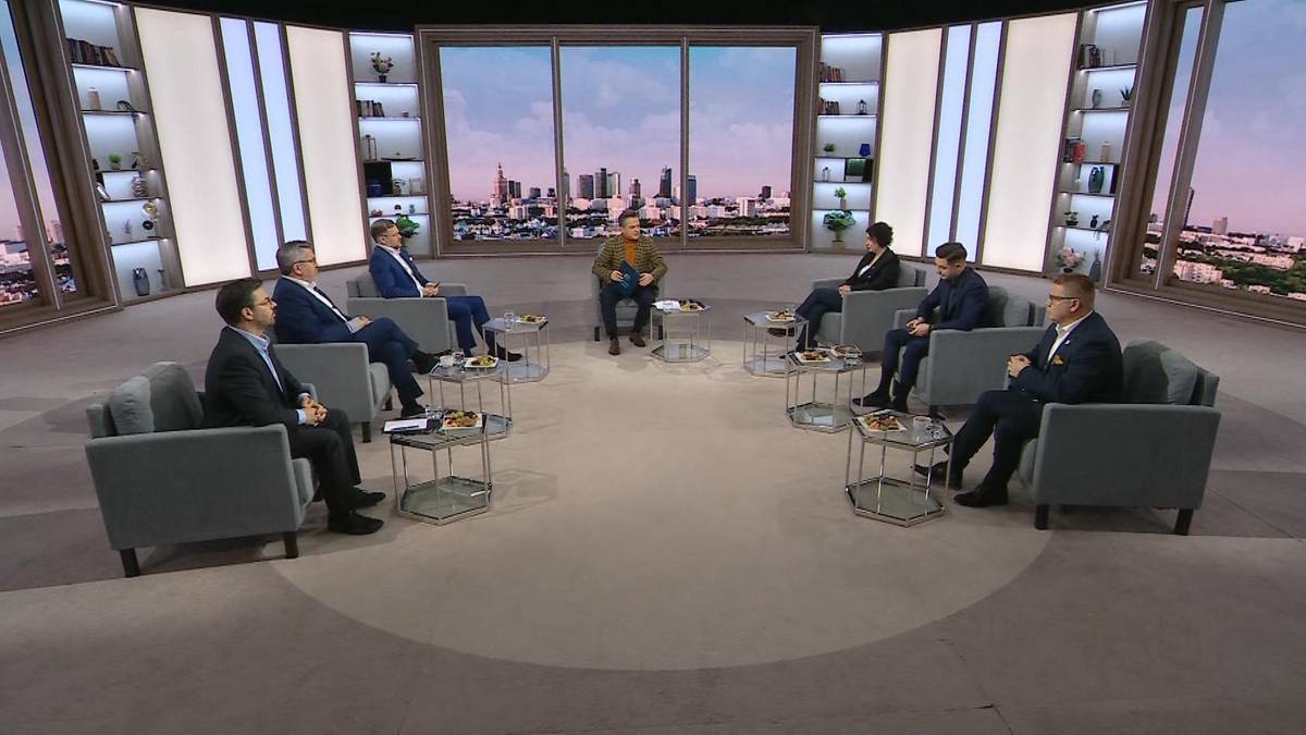 Grupa mężczyzn w garniturach siedzi w studio telewizyjnym, dyskutując przy okrągłym stoliku.