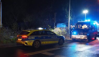 Dwa radiowozy policyjne z włączonymi niebieskimi i czerwonymi sygnałami świetlnymi na miejscu wypadku nocą.