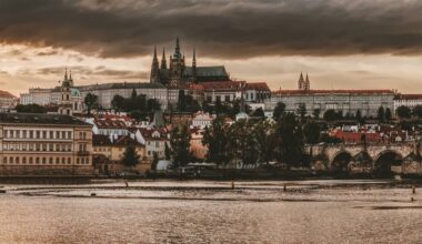 Panorama Pragi z widocznym Zamkiem na Hradczanach i mostami nad Wełtawą pod zachmurzonym niebem.