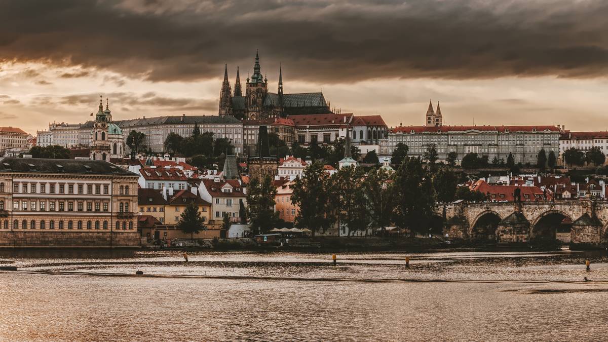 Panorama Pragi z widocznym Zamkiem na Hradczanach i mostami nad Wełtawą pod zachmurzonym niebem.