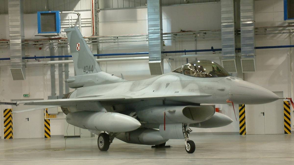 Szary samolot myśliwski F-16 z polskimi oznaczeniami w hangarze