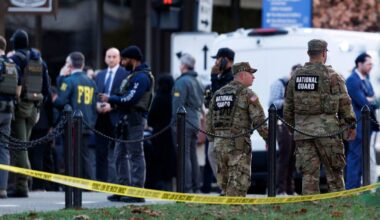 Grupa umundurowanych funkcjonariuszy FBI i Narodowej Gwardii stoi za żółtą taśmą zabezpieczającą.