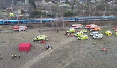 Miejsce katastrofy kolejowej z licznymi pojazdami ratowniczymi i dwoma pociągami na torach.