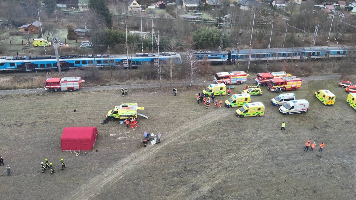 Miejsce katastrofy kolejowej z licznymi pojazdami ratowniczymi i dwoma pociągami na torach.