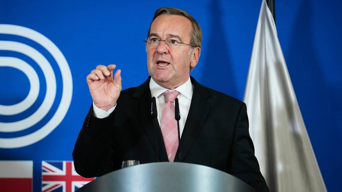 Boris Pistorius, niemiecki minister obrony, przemawia za mównicą na tle banera i flag państwowych.