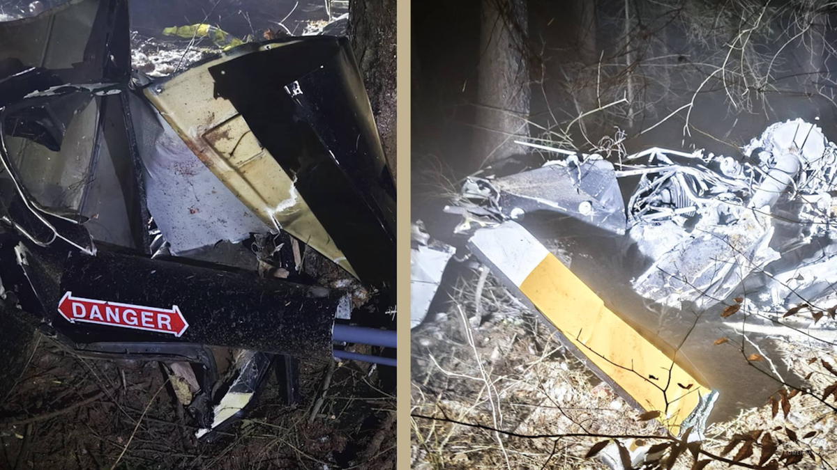 Fragmenty rozbitego śmigłowca leżące wśród drzew i gałęzi.